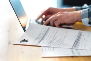 Young man writing college or university application form with laptop. Student applying to school.