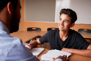 High School Tutor Giving Male Student One To One Tuition At Desk